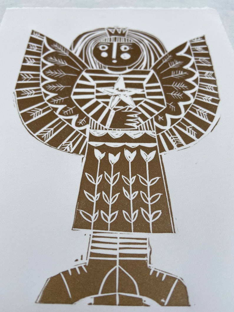 May include: A brown and white linocut print of an angel holding a star. The angel has a crown, a striped dress, and a skirt with flowers. The angel's wings are made of stylized pine branches.
