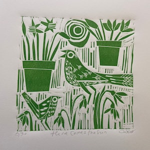 Op de afbeelding: Een groene linosnede van een vogel die in een tuin zingt met de tekst "Here Comes the Sun" en de handtekening van de kunstenaar "Audrey".
