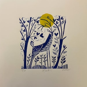 May include: A blue and yellow linocut print of a deer standing in a forest with a yellow sun in the background. The print is signed "Haat." and numbered "5/30".