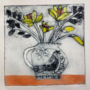 May include: An art print of daffodils in a decorative vase. The vase features a bird design. The daffodils are yellow with orange centres. The print is on a white background with an orange table.