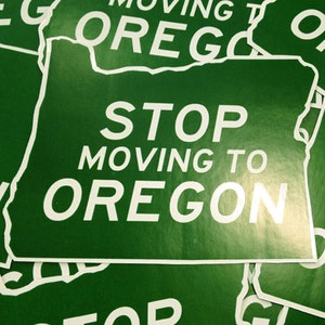 May include: A green sign with the text "STOP MOVING TO OREGON" in white letters. The sign is shaped like the state of Oregon.