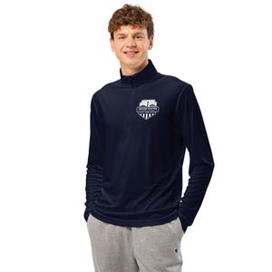 Peut inclure: Chemise marine à manches longues et fermeture éclair quart de zip, avec un emblème blanc sur la poitrine. L'emblème comporte les mots "UNITED STATES" et un motif de bouclier. La chemise est faite d'une matière douce et confortable.