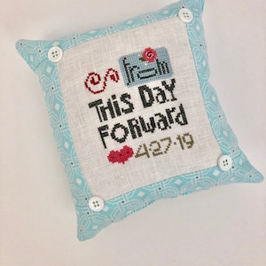 May include: A white pillow with a blue and white patterned border. The pillow has a cross-stitch design that says "Go Fresh This Day Forward" with a heart and the date "4.27.19".