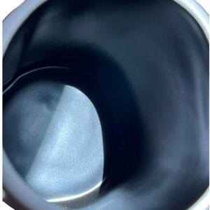 May include: Close-up of a white and black ceramic mug. The interior is dark, with a glossy finish. The rim of the mug is white and has a slightly irregular shape. The mug appears to be empty.