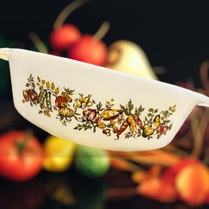 May include: White ceramic baking dish with a floral design featuring vegetables and mushrooms. The dish has two handles on the sides.