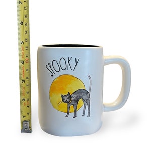 May include: White ceramic mug with a black interior, featuring the word "SPOOKY" above a watercolor illustration of a black cat in front of a yellow moon. The mug is approximately 4 inches tall.