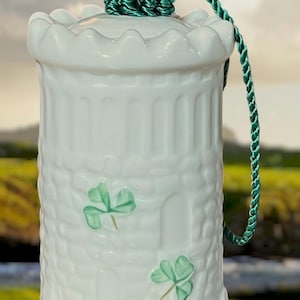 May include: White ceramic jar with a lid and green rope handle. The jar features a textured design with shamrock accents. The jar is cylindrical with a scalloped rim and a green rope handle.