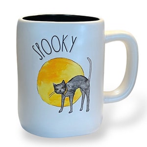 May include: White ceramic mug with a black interior and a large handle. The mug features the word "SPOOKY" in black script above a watercolor illustration of a black cat with a yellow collar in front of a yellow circle.