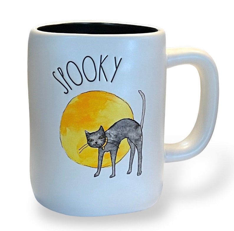 May include: White ceramic mug with a black interior and a large handle. The mug features the word "SPOOKY" in black script above a watercolor illustration of a black cat with a yellow collar in front of a yellow circle.