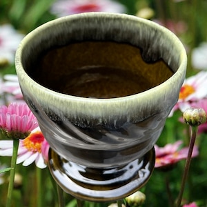 May include: A dark green and light green glazed ceramic planter with a swirl design. The planter has a wide, round opening and a small, round base.