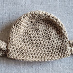May include: A crocheted hat with two ear flaps, made in a beige color.
