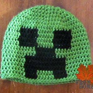May include: Green crocheted hat with a black Minecraft Creeper face design.