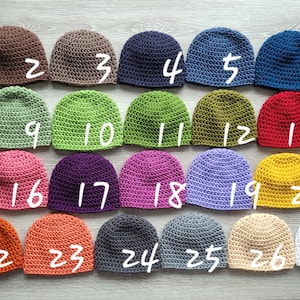May include: Twenty-seven crocheted hats in various colors, numbered 1 through 27. The hats are arranged in rows on a wooden surface.