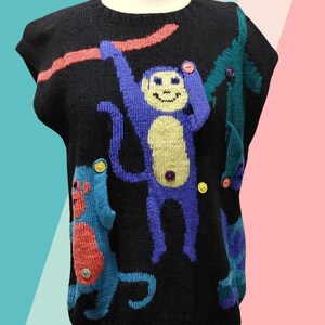 May include: Black sleeveless sweater featuring a playful monkey design. The sweater has a crew neck and is adorned with colorful monkeys in blue, teal, and red, with button accents. The sweater is displayed on a mannequin.