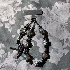 May include: A black beaded bracelet with clear and iridescent beads, and a gun-shaped charm. The bracelet features large, clear, faceted beads and smaller black beads. The gun charm is black and detailed.