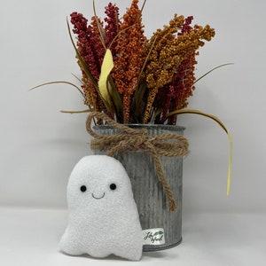 May include: A white plush ghost with a smiling face sits in front of a metal tin can filled with dried flowers. The tin can has a brown twine bow and a label that reads "Life is Fresh".