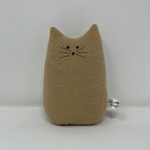 May include: A tan plush cat toy with black embroidered eyes and whiskers. The toy has a white tag with the text "Little Branch" in green.