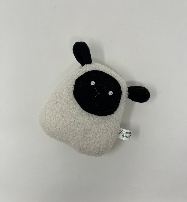 Pode incluir: Brinquedo de pel&uacute;cia branco em forma de ovelha com orelhas pretas e um rosto preto. O brinquedo tem dois olhos de bot&atilde;o branco e uma pequena boca preta costurada. O brinquedo tem uma etiqueta verde que diz "Life is Fresh".