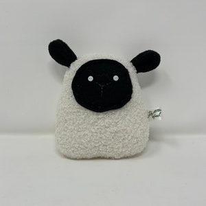 Pode incluir: Um brinquedo de pel&uacute;cia de ovelha branco com orelhas pretas, um rosto preto e olhos de bot&atilde;o brancos. O brinquedo tem uma pequena etiqueta verde com o texto "Little Fresh" nela.