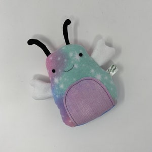 May include: A plush toy shaped like a bug with a light blue, pink, and white starry pattern. The bug has black antennae, white wings, and a purple belly. The toy has a small tag that says "Little Sprout".