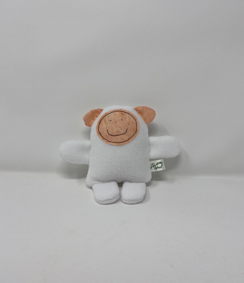 May include: White plush toy with a brown felt face and a smiling mouth. The toy has small ears and arms and is sitting on a white surface. The toy has a green tag with the text "Little Sprout" on it.