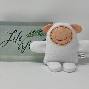 May include: White plush toy with a brown felt face and a smiling mouth. The toy has small ears and arms and is sitting on a white surface. The toy has a tag that says "Life/After/Life".