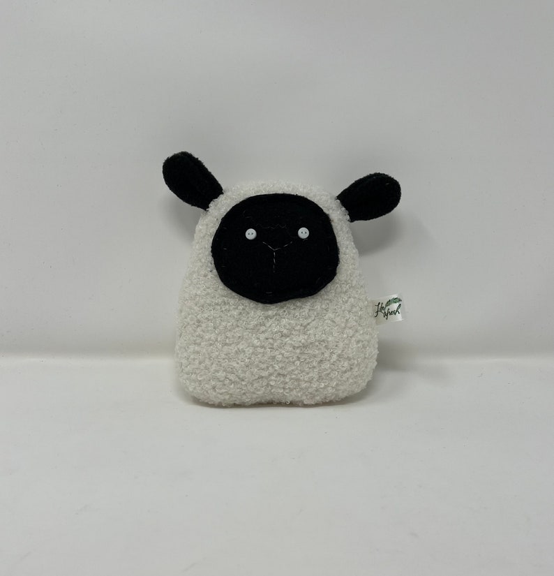 Pode incluir: Brinquedo de pel&uacute;cia branco em forma de ovelha com orelhas, rosto e olhos pretos. O brinquedo tem uma pequena etiqueta que diz "Happy Owl".