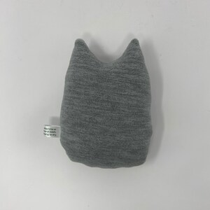 May include: Gray plush cat-shaped pillow with a white tag that reads "Machine or hand wash, hang to dry."