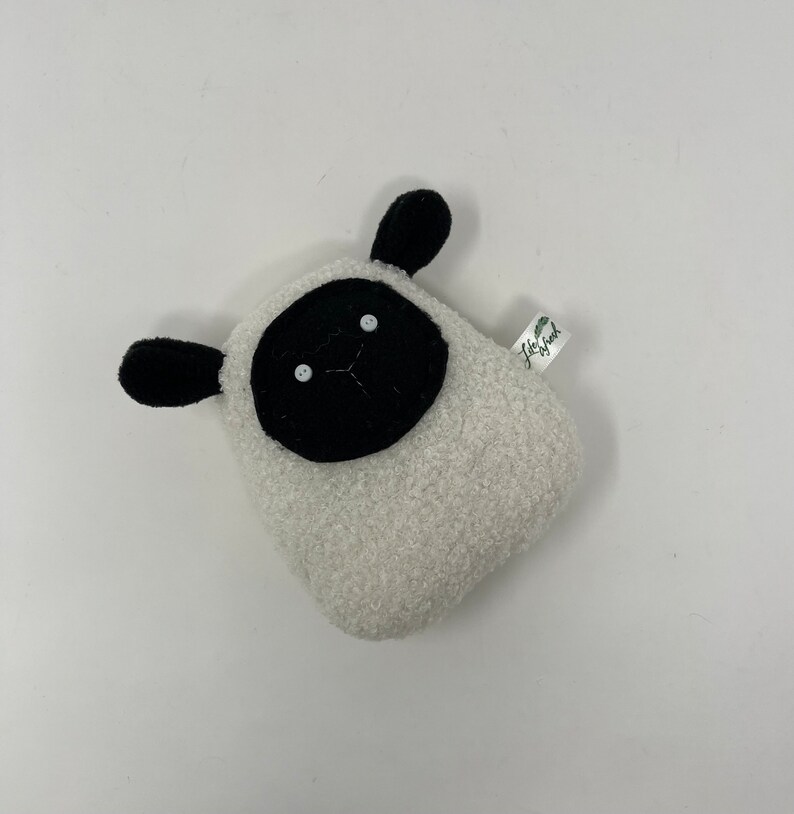 Pode incluir: Brinquedo de pel&uacute;cia branco em forma de ovelha com rosto e olhos de feltro preto. O brinquedo tem uma pequena etiqueta que diz "Little Good".