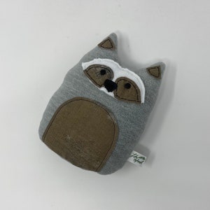 May include: Gray plush raccoon stuffed animal with a white face and black eyes. The stuffed animal has a brown belly and a tag that says "Little Sprout".