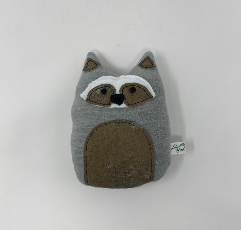 May include: Gray plush raccoon stuffed animal with a brown belly and black eyes. The stuffed animal has a white patch on its face and a small green tag that says "Little Sprout".