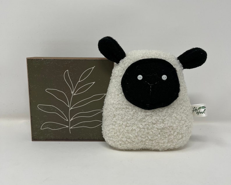 Pode incluir: Brinquedo de pel&uacute;cia branco em forma de ovelha com orelhas, rosto e nariz pretos. A ovelha tem dois olhos de bot&atilde;o brancos. O brinquedo tem uma pequena etiqueta que diz "Little Sheep".