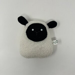Pode incluir: Brinquedo de pel&uacute;cia de ovelha branca com orelhas, rosto e olhos pretos. O brinquedo tem uma pequena etiqueta verde com o texto "Little Sheep" nela.
