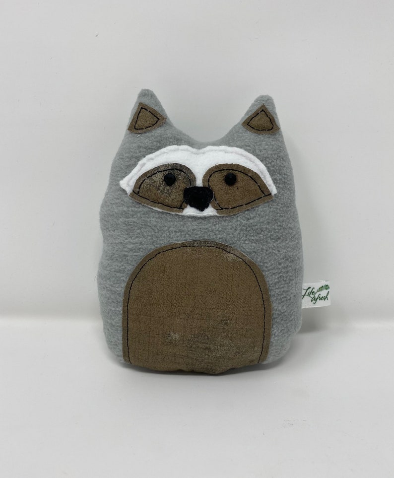May include: Gray plush raccoon stuffed animal with black eyes, a white nose, and brown ears. The raccoon has a brown belly patch and a small tag that says "Lily & Jack".