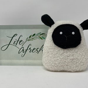 Pode incluir: Brinquedo de pel&uacute;cia branco em forma de ovelha com orelhas, rosto e olhos pretos. O brinquedo tem uma etiqueta que diz "Life A Fresh".