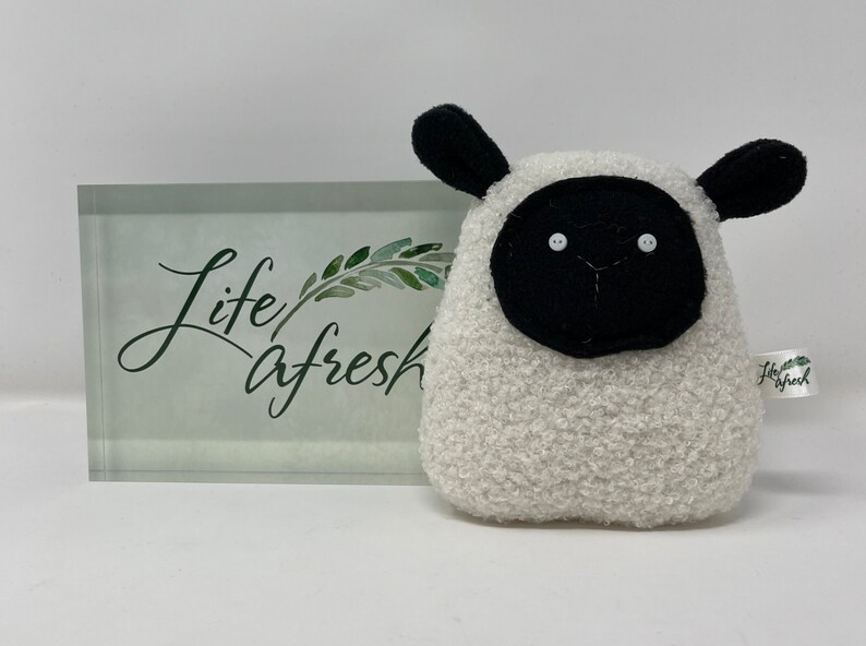 Pode incluir: Brinquedo de pel&uacute;cia branco em forma de ovelha com orelhas, rosto e olhos pretos. O brinquedo tem uma etiqueta que diz "Life A Fresh".