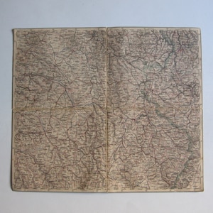 Op de afbeelding: Een vintage kaart van een regio met gedetailleerde lijnen en markeringen, waarschijnlijk ter aanduiding van wegen, rivieren en steden. De kaart is gedrukt op verouderd papier en heeft een versleten uiterlijk.