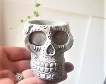 May include: White ceramic skull planter with detailed sugar skull design. The planter is small and has a hole in the bottom for drainage.