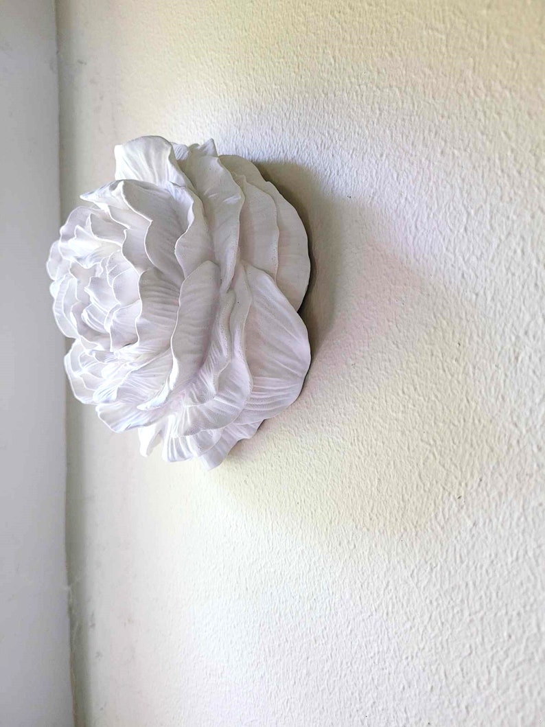 Puede incluir: Una escultura de pared de cer&aacute;mica blanca de una gran flor estilizada con m&uacute;ltiples capas de p&eacute;talos.