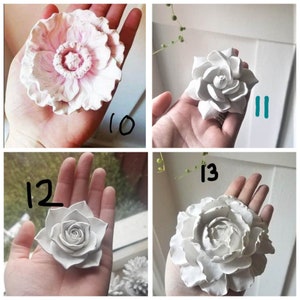Puede incluir: Cuatro decoraciones de flores de cer&aacute;mica blanca. Las flores est&aacute;n en diferentes etapas de floraci&oacute;n, algunas tienen m&aacute;s p&eacute;talos que otras. Las flores son todas blancas y tienen una superficie ligeramente texturizada.
