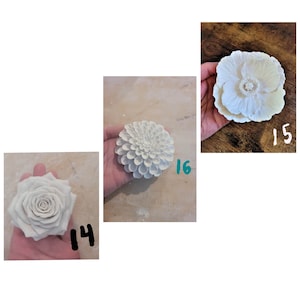 Puede incluir: Tres esculturas de flores de cer&aacute;mica blanca. La primera es una rosa, la segunda es una dalia y la tercera es una amapola.