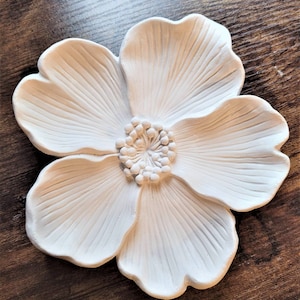 May include: White ceramic flower wall decor with a raised center and five petals. The flower has a textured surface and a detailed center.
