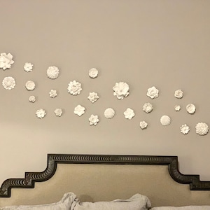 Puede incluir: Una cabecera blanca con un dise&ntilde;o decorativo y una pared decorada con flores blancas.