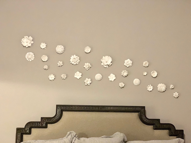Puede incluir: Una cabecera blanca con un dise&ntilde;o decorativo y una pared decorada con flores blancas.