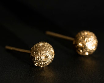 May include: A pair of gold-toned stud earrings with a textured, spherical design.