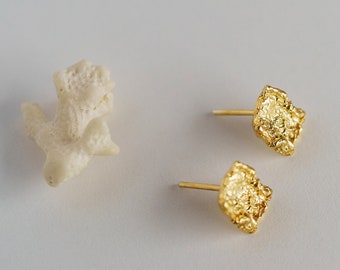May include: A pair of gold-toned earrings with a textured, irregular square shape. The earrings are on a white surface.