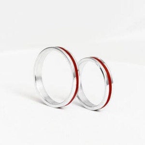 Peut inclure: Deux bagues en argent avec une fine ligne rouge autour du bord.