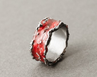 May include: A silver ring with a red enamel band. The band has a textured, irregular edge.