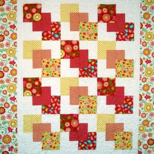 May include: A white quilt with a patchwork design featuring red, yellow, and floral patterned squares. The quilt has a white background and a floral border.