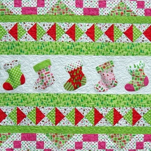 May include: A Christmas quilt with a red, white, and green color scheme. The quilt features a variety of patterns, including stockings, trees, and candy canes.